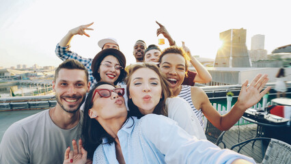 Point of view shot of happy friends taking selfe on roof at summer party laughing, posing and...