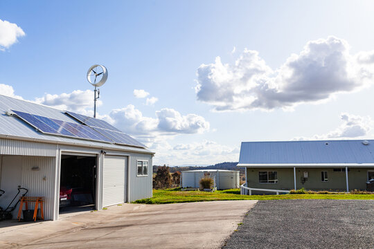 sustainable off grid living with solar power and wind turbine on roof beside farm house