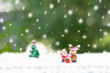 santa doll, reindeer and presents with snow decorated  background green nature. concept christmas celebration, santa claus deliver presents on snowy day