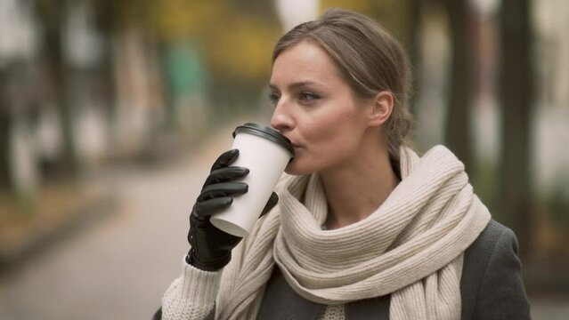 This is a close up profile picture of young and beautiful girl standing in city pedestrians avenue with take a way coffee cup in her hands.