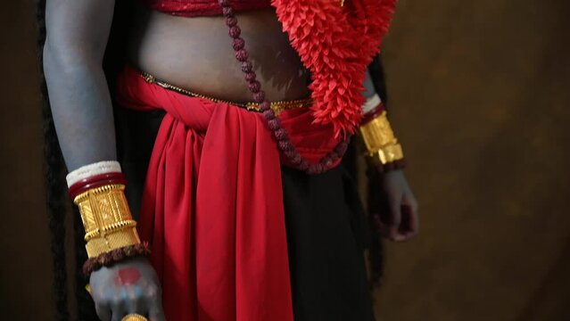 Man dressed as angry Indian Goddess Kali looks at camera, Indian goddess cosplay with long hair and dark background, slow tilt body reveal shot