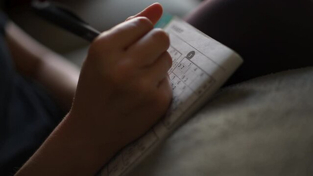 Close up of a page in a Sudoku puzzle book as a woman's hand fills in the numbers. Shallow depth of field.