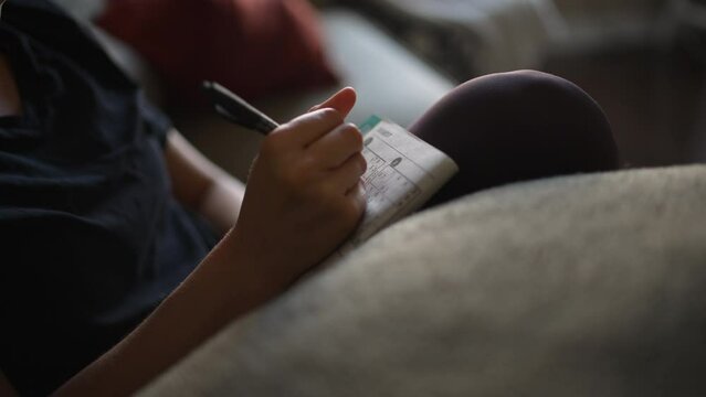 Close up of a woman's hand as she fills in a Sudoku puzzle at home while sitting on the couch.