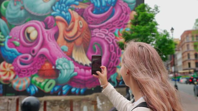 Person holding cell phone taking a photo of mural in a city