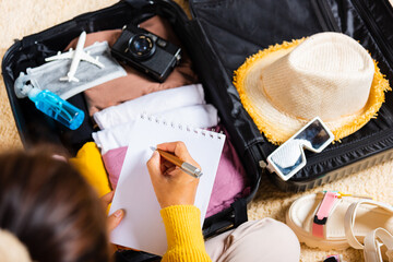 Woman writing paper take note and packing suitcase to vacation writing paper list sitting on room