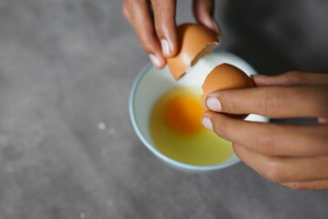 someone is breaking eggs to make omlette on a concrete background