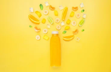 Rolgordijnen Bottle of orange fruit juice under cutted different fruits and ice in yellow background © Anastasija Grinuka/Wirestock Creators