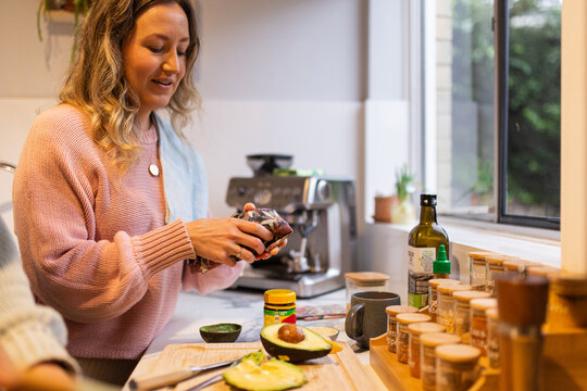 woman opening a beeswax wrap in the kitchen with avocado and spices on the bench