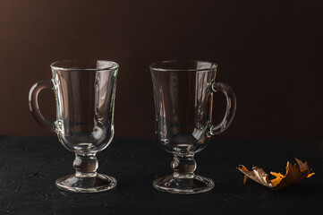 Two empty glass glasses for hot drinks on a dark background and a dried autumn leaf.