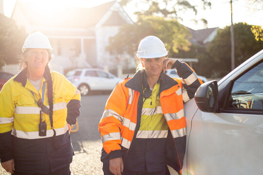 Two smiling women road workers wearing white helmet with orange and yellow jacket on sunset sunrise