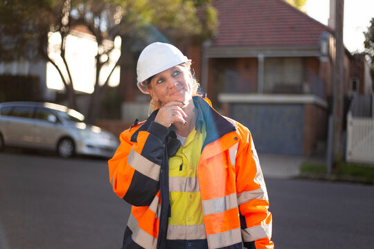 Woman road worker looking up with a white helmet and orange jacket with silver reflector on it