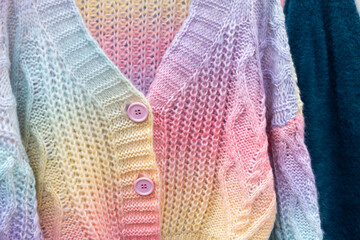 Close up of colorful knitted sweaters with buttons. Bunch of clothes of different colors for sale. Cheep clothing and fast fashion theme