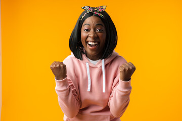 Portrait of an excited young african woman celebrating success against yellow background
