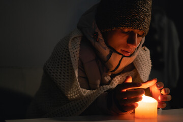 Young man without electricity at home with candle. Shutdown of heating and electricity, power...