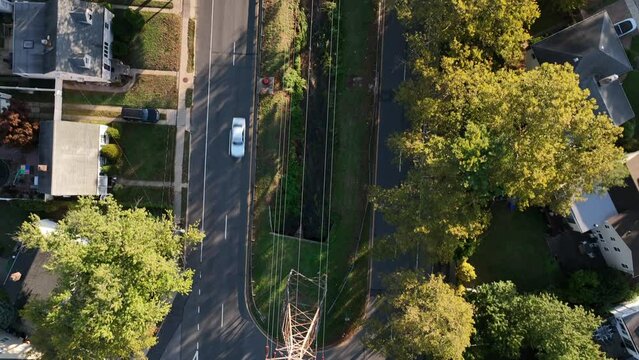 Aerial top view of a transmission tower near a road in a green suburban neighborhood on a sunny day