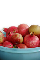 Many ripe red Pomegranate fruits in plastic bowl against white background. Punica granatum harvest 