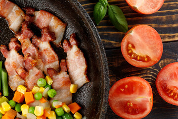 Fried bacon with vegetables and tomatoes in a pan.