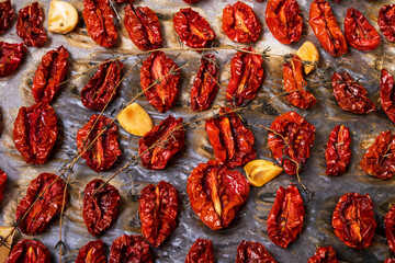 Close-up top view oven-roasted sundried tomatoes on a baking sheet on parchment paper with garlic, thyme and olive oil. Selective focus.