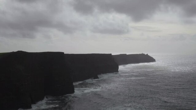 Cliffs of Moher silhouetted with moody dark weather clouds and crashing Atlantic sea, Ireland.