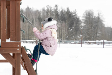 a child on a playground in winter climbs a rope