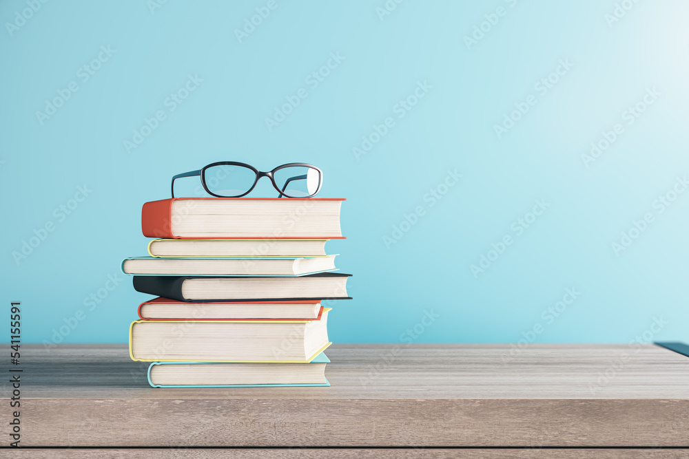Poster close up of stacked books and glasses on blurry blue background with mock up place. school and educa