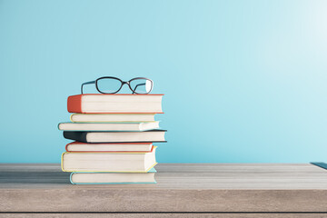 Close up of stacked books and glasses on blurry blue background with mock up place. School and...