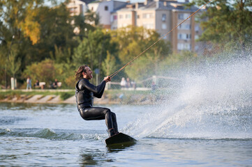 Wakeboarder making tricks while wakeboarding on lake. Young man surfer having fun wakesurfing in the cable park. Water sport, outdoor activity concept.