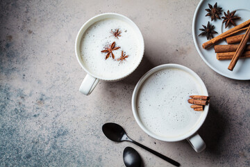 Homemade chai latte with cinnamon and star anise in white cup, dark background.