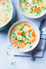 Fish cod chowder soup with green peas, potatoes and carrots in white bowl.