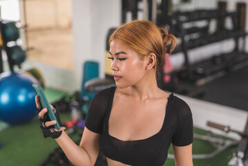 A sexy young filipino asian woman chatting with someone on her phone in between sets at the gym.