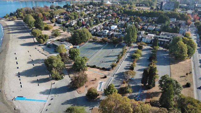 Drone shot of Kitsilano in Vancouver, British Columbia showing residential homes, condo apartment, beach, city skyline, tennis court and trees.