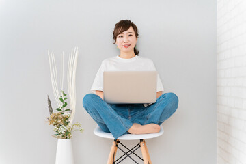 新生活で椅子に座りながらパソコンを使うおしゃれなアジア人女性（笑顔）
