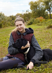 Naklejka na ściany i meble a joyful woman is sitting on the grass with her Labrador retriever dog and enjoying an autumn vacation 