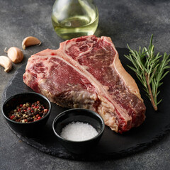 Raw porterhouse steak with spices lying on a dark grey table. Raw fresh beef T-bone steak.