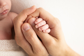 A newborn holds on to mom's, dad's finger. Hands of parents and baby close up. A child trusts and holds her tight. Tiny fingers of a newborn. The family is holding hands. Concepts of family and love.