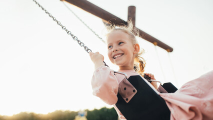 Cute little girl swinning on a swing on the playground at sunset.