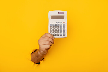 Male hand with calculator through a paper hole in yellow background