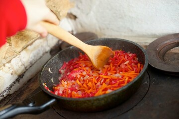 Frying vegetables on a wood-burning stove for cooking the first course, soup or borscht.