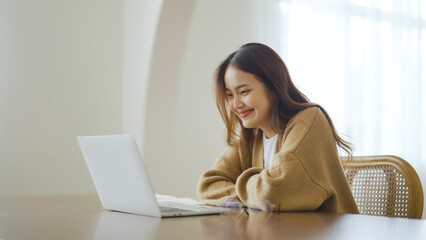Smiling asian young woman working on laptop at home office. Young asian student using computer remote studying, virtual training, e-learning, watching online education webinar at house