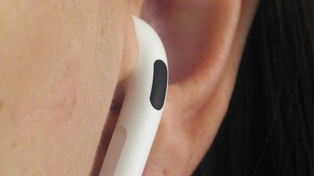 Close-up human ear with a white wireless earphone. A man listens to music with headphones. macro video.