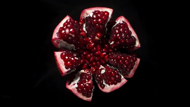 a torn Pomegranate rotates on a black background, red grains, top view.