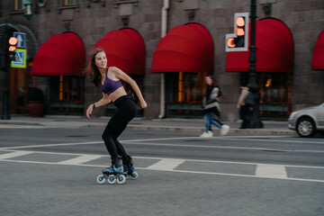 Slim sporty young woman uses rollerskates as mode of transportation in city enjoys favorite hobby...