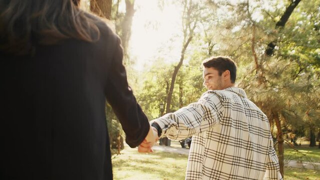 Young guy taking his girlfriend by the hand on a walk in the park. Sun shining in front of them. Follow me concept