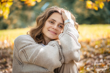 Beautiful caucasian young woman in a beige sweater enjoying nature and fresh air sitting in an...