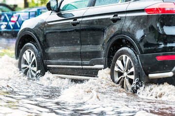The car is driving through a puddle in heavy rain. Splashes of water from under the wheels of a...