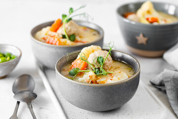 Soup with meatballs, cauliflower, baby peas, carrots and cream on a white background.