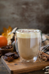 Seasonal autumn concept with drink. Glass of latte macchiato coffee, warm scarf and maple leaves on rustic background. Copy space.