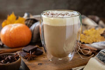 Seasonal autumn concept with hot drink. Pumpkin latte spice coffee, warm scarf and maple leaves on rustic background.