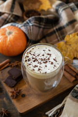 Seasonal autumn concept with drink. Glass of latte macchiato coffee, warm scarf and maple leaves on rustic background.
