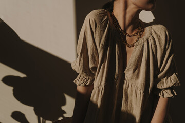 Young pretty woman in neutral beige linen sundress, dress in sun light shadows. Elegant luxury...